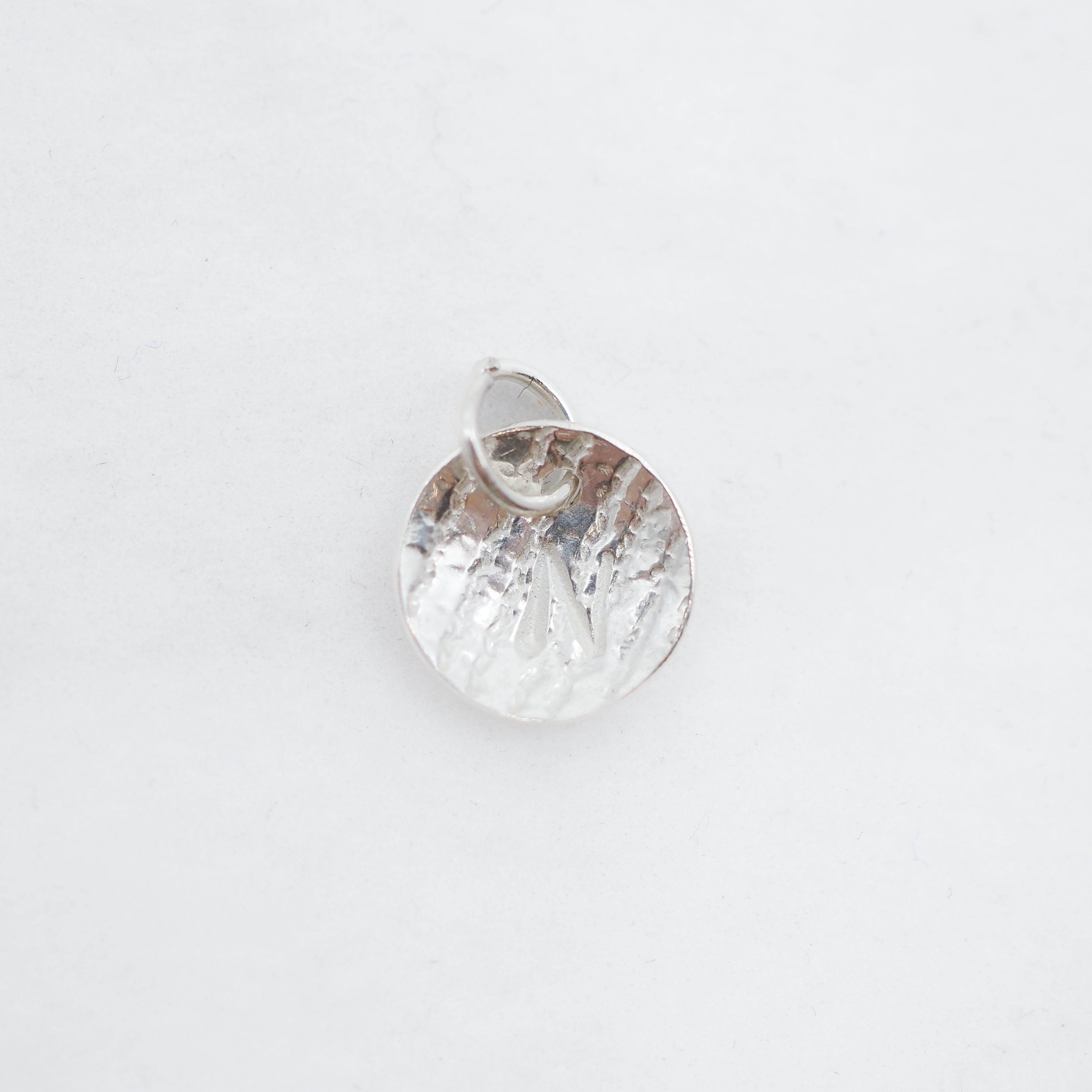 A small hammered silver pendant charm with a textured, organic surface and a top loop, shown on a plain white background.