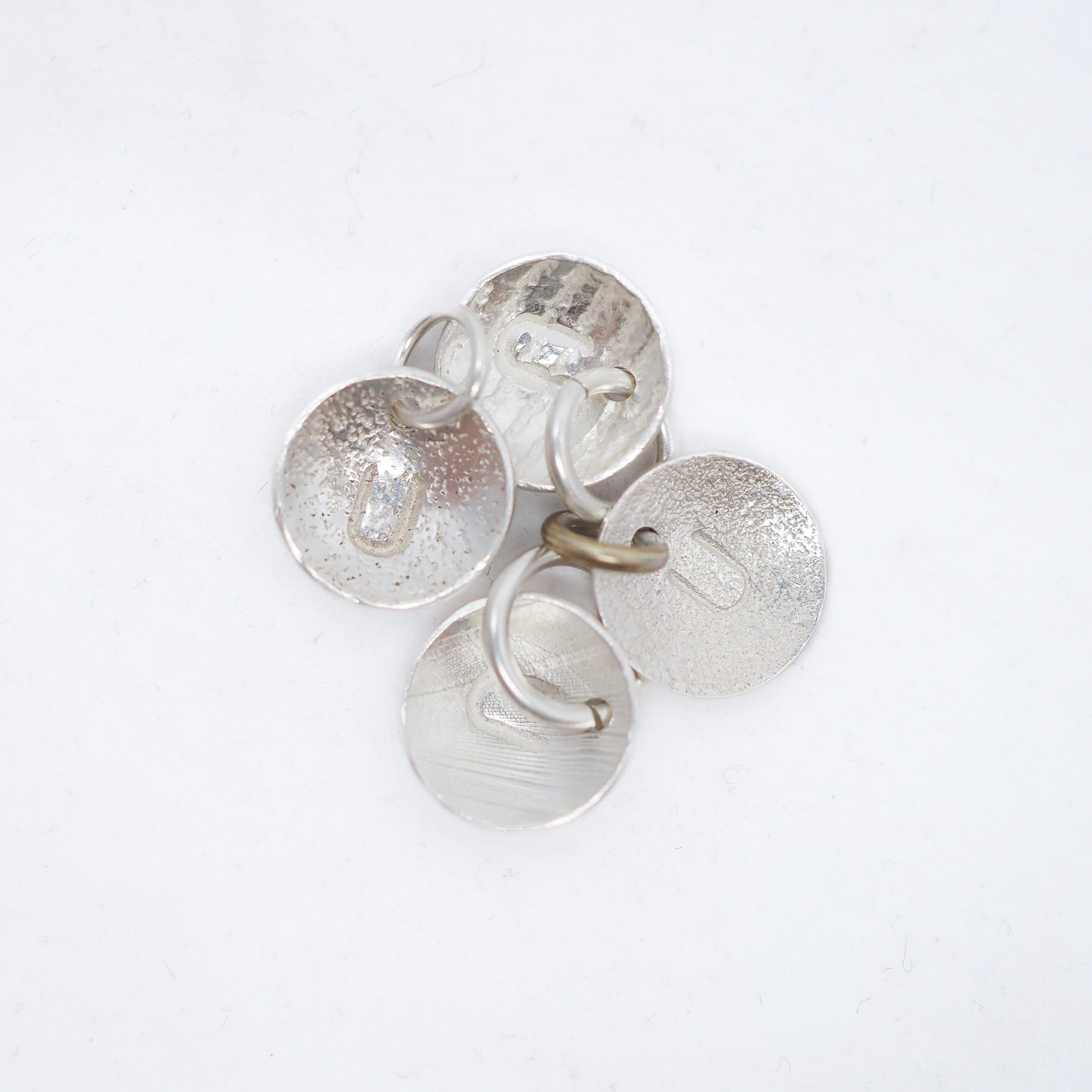 A cluster of five textured silver disc charms with small metal loops, arranged on a plain white background.