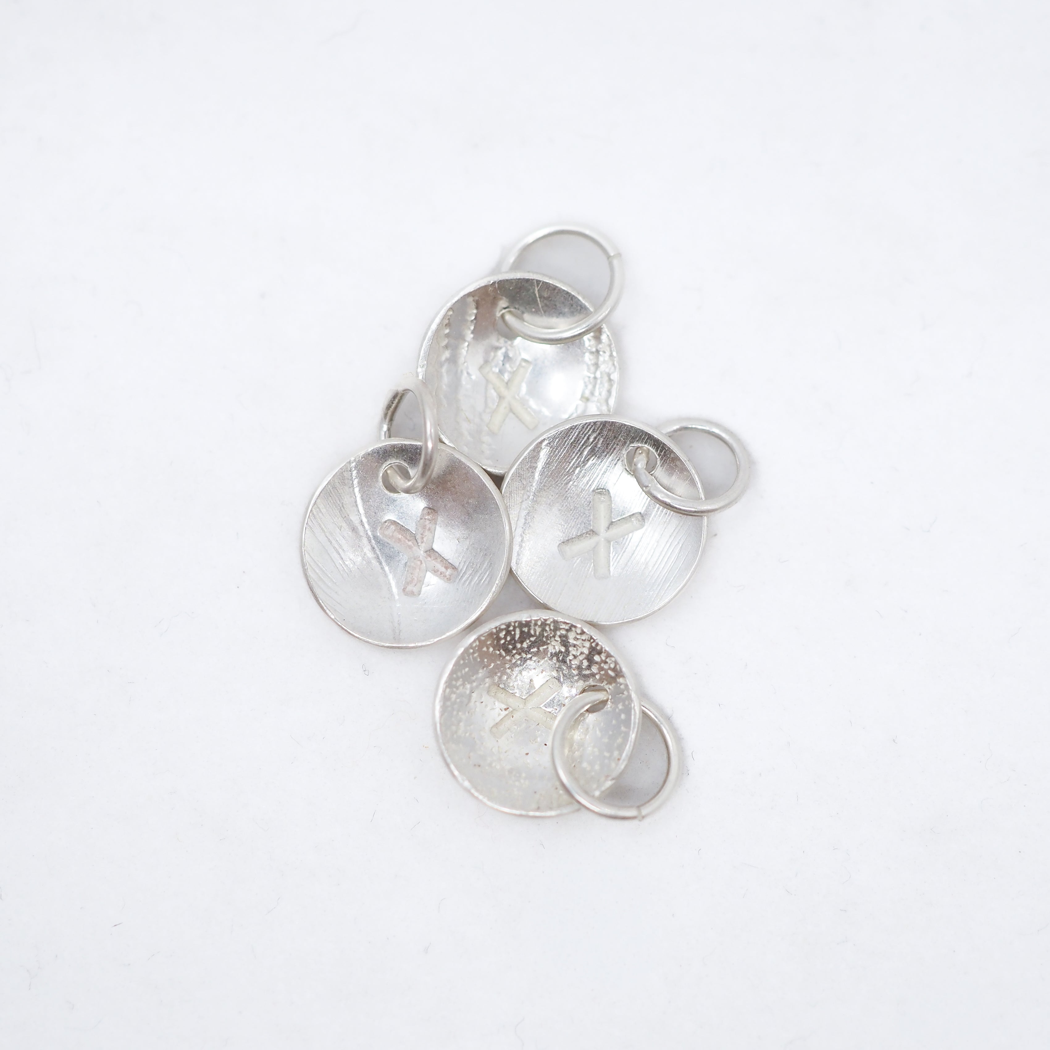 Five textured silver circular jewelry charms with small jump rings, arranged on a plain white background.
