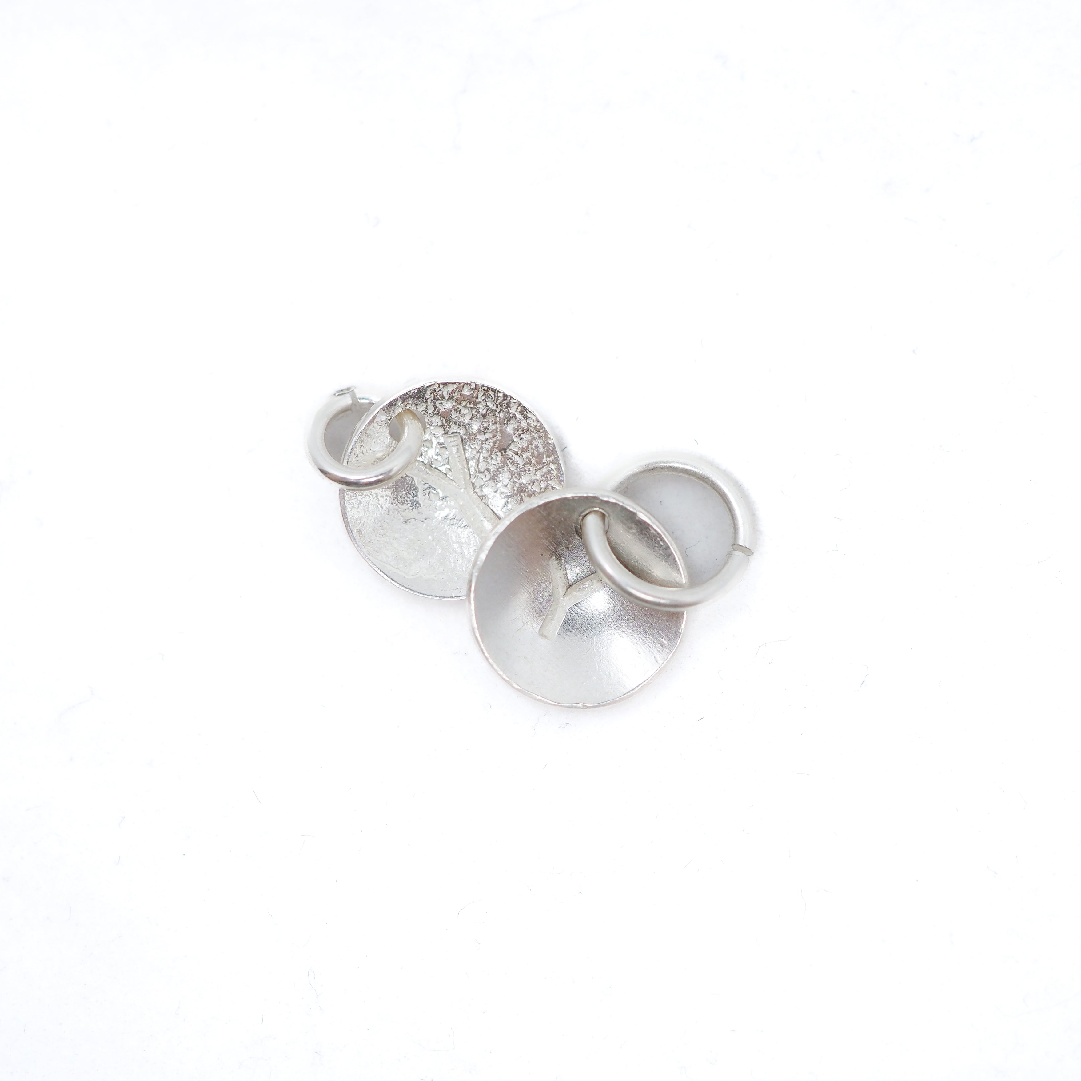 Three silver metal jewelry findings, including a textured disc, a flat disc, and a small ring, arranged on a plain white background.