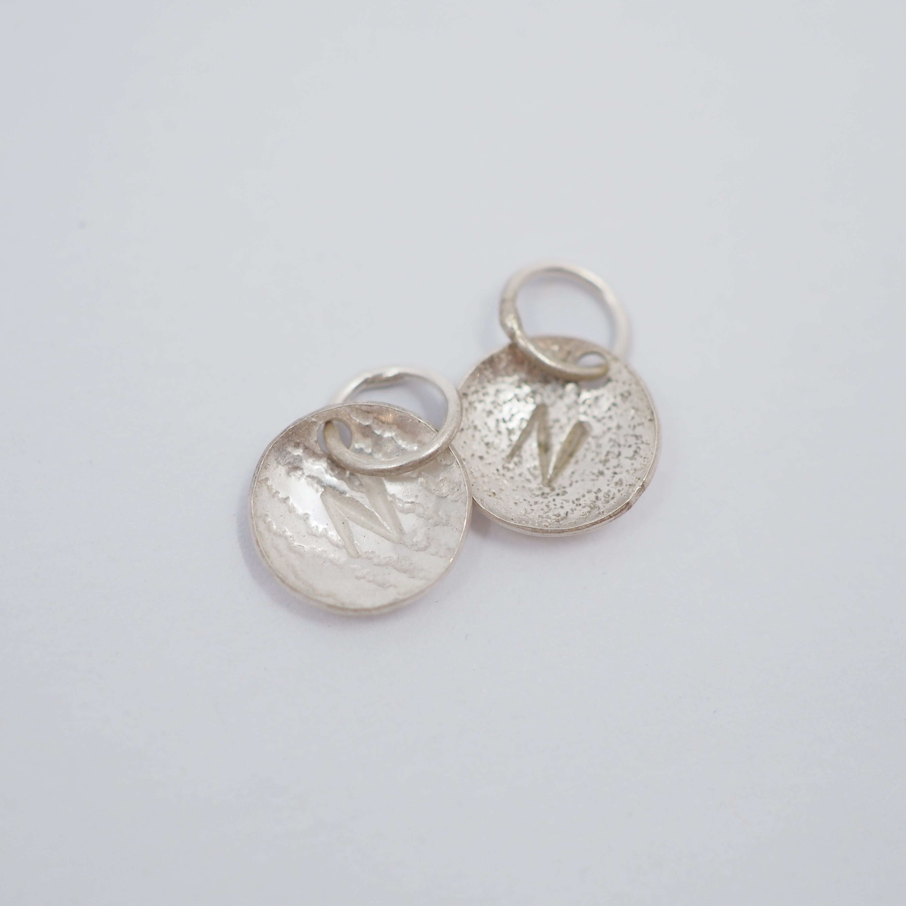 Two textured silver disc charms with engraved letter 'N' and jump rings, displayed on a light gray background.