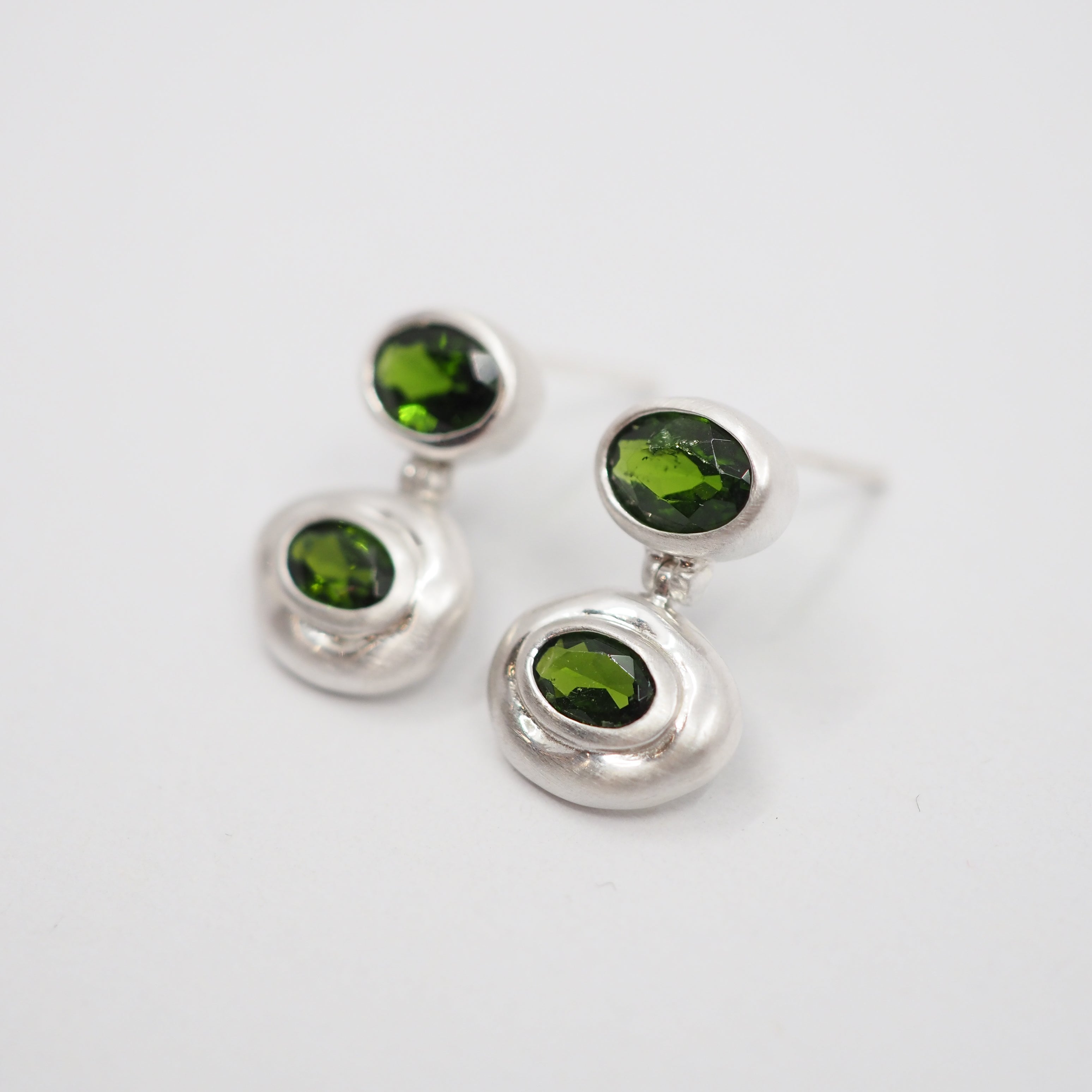 A pair of silver dangle earrings with oval-cut green gemstones, displayed on a clean white background.