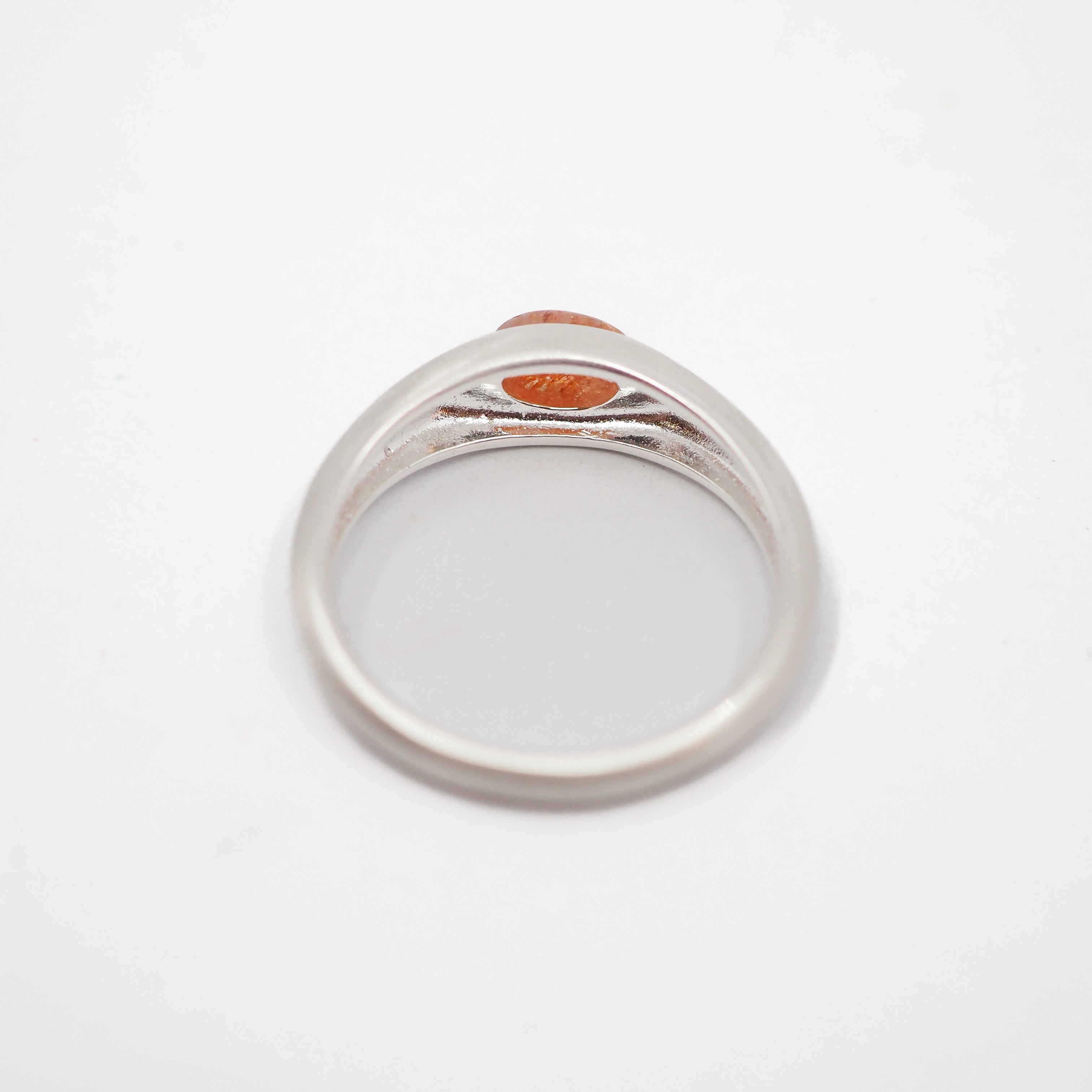 A silver-toned signet ring with a small oval orange stone, photographed from above on a plain white background.