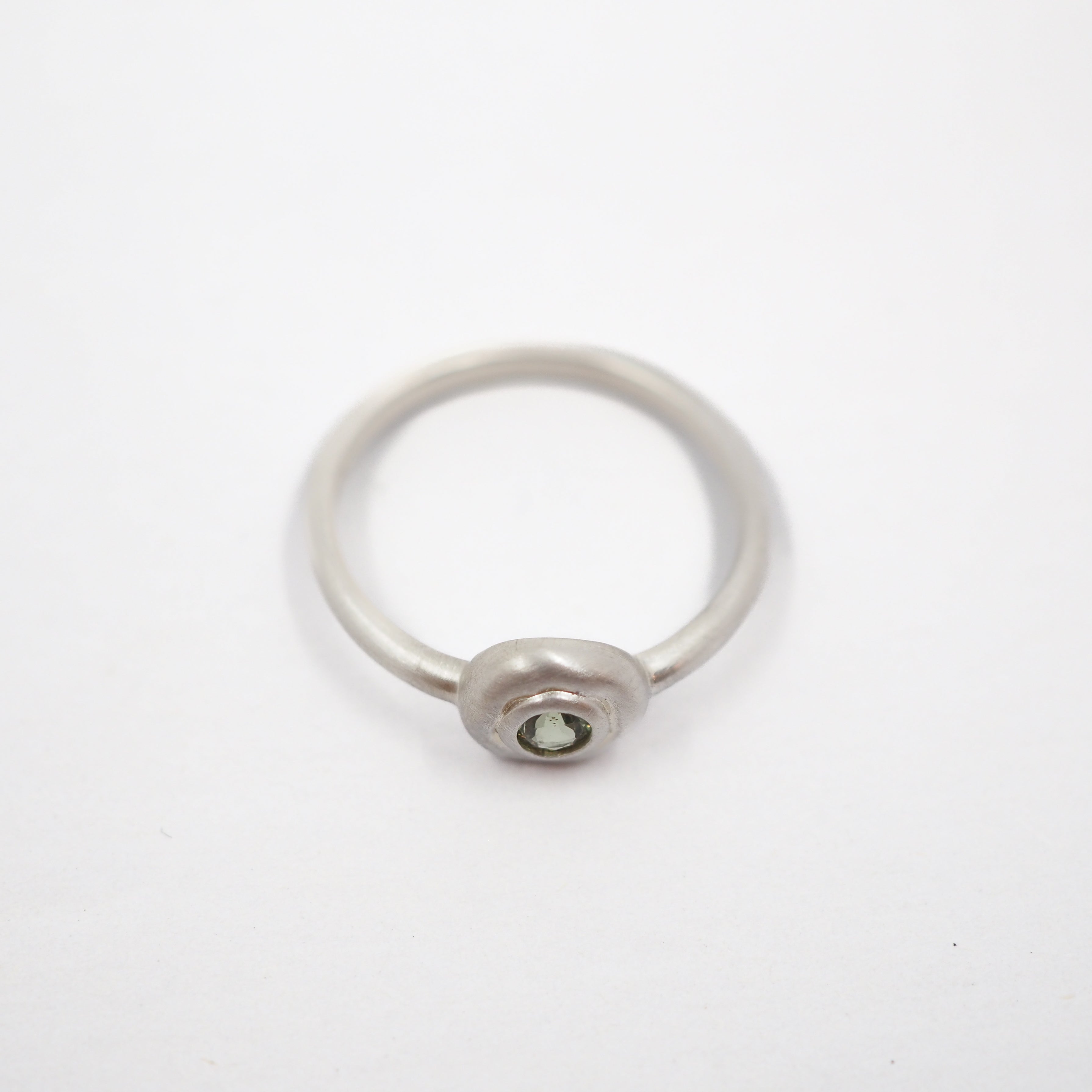 A minimalist silver ring with a small oval bezel containing a clear round gemstone, set against a plain white background.