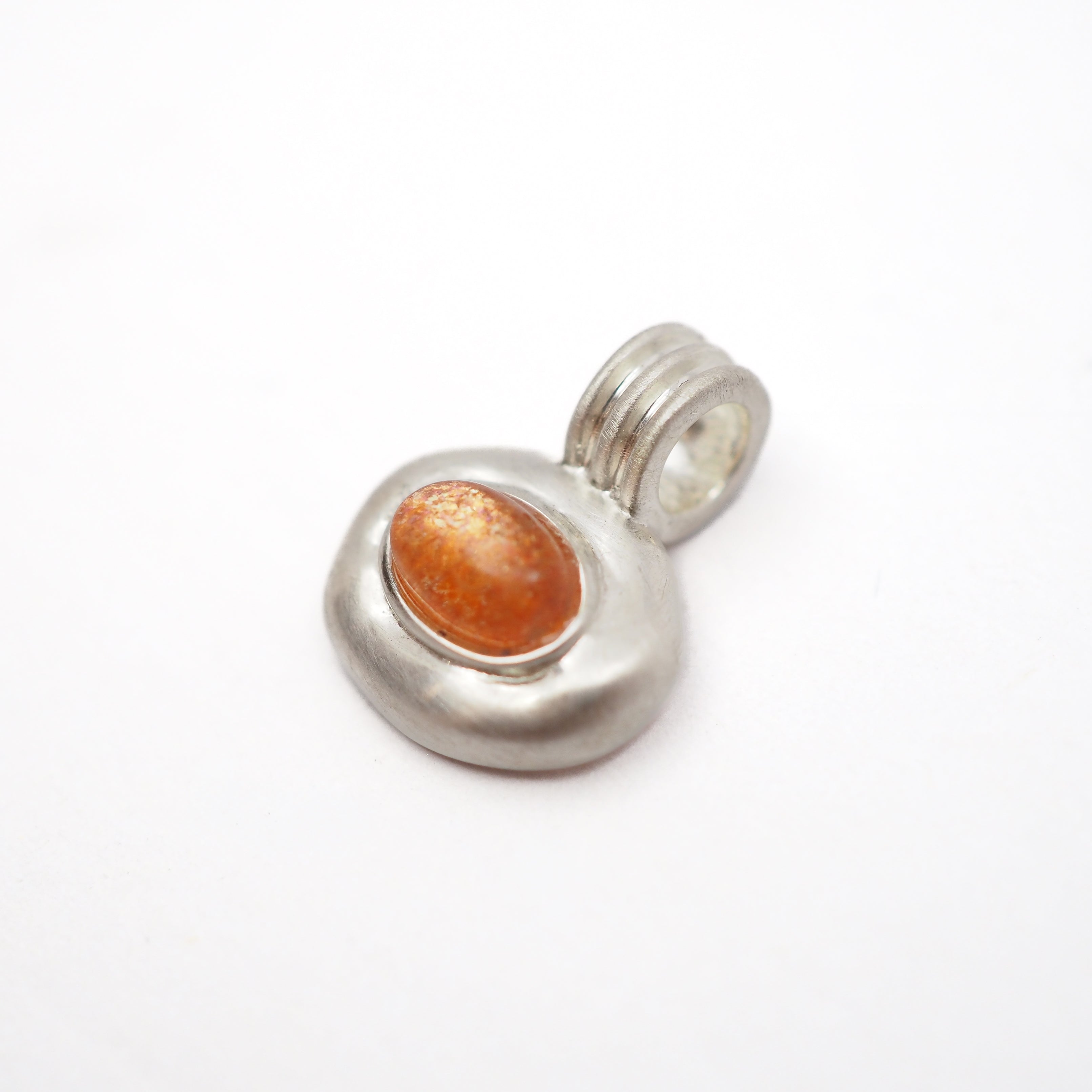 A sterling silver pendant featuring a textured, organic-shaped bezel set with a smooth, oval orange cabochon gemstone, shown on a plain white background.