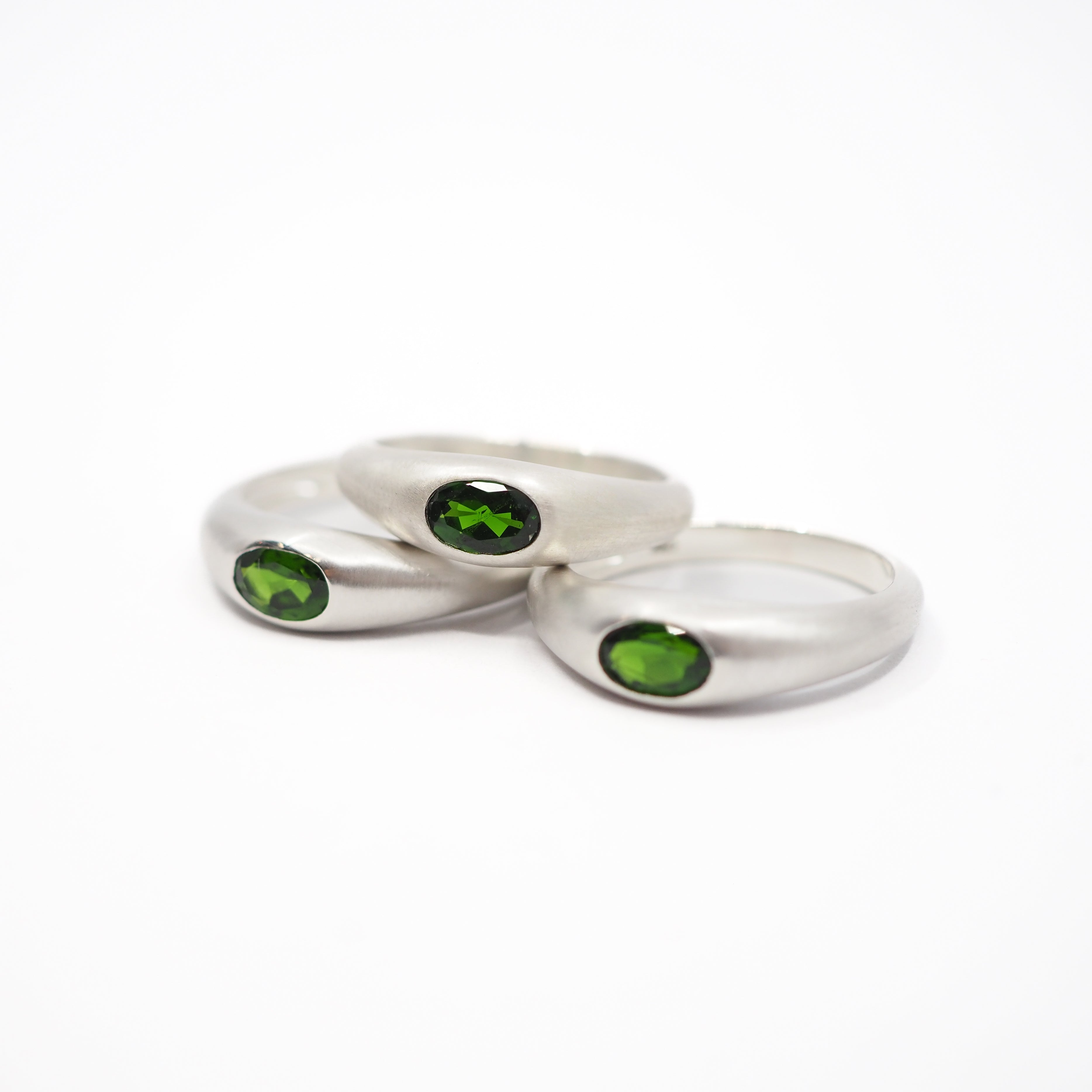 Three silver rings with oval green gemstones, arranged on a plain white background.
