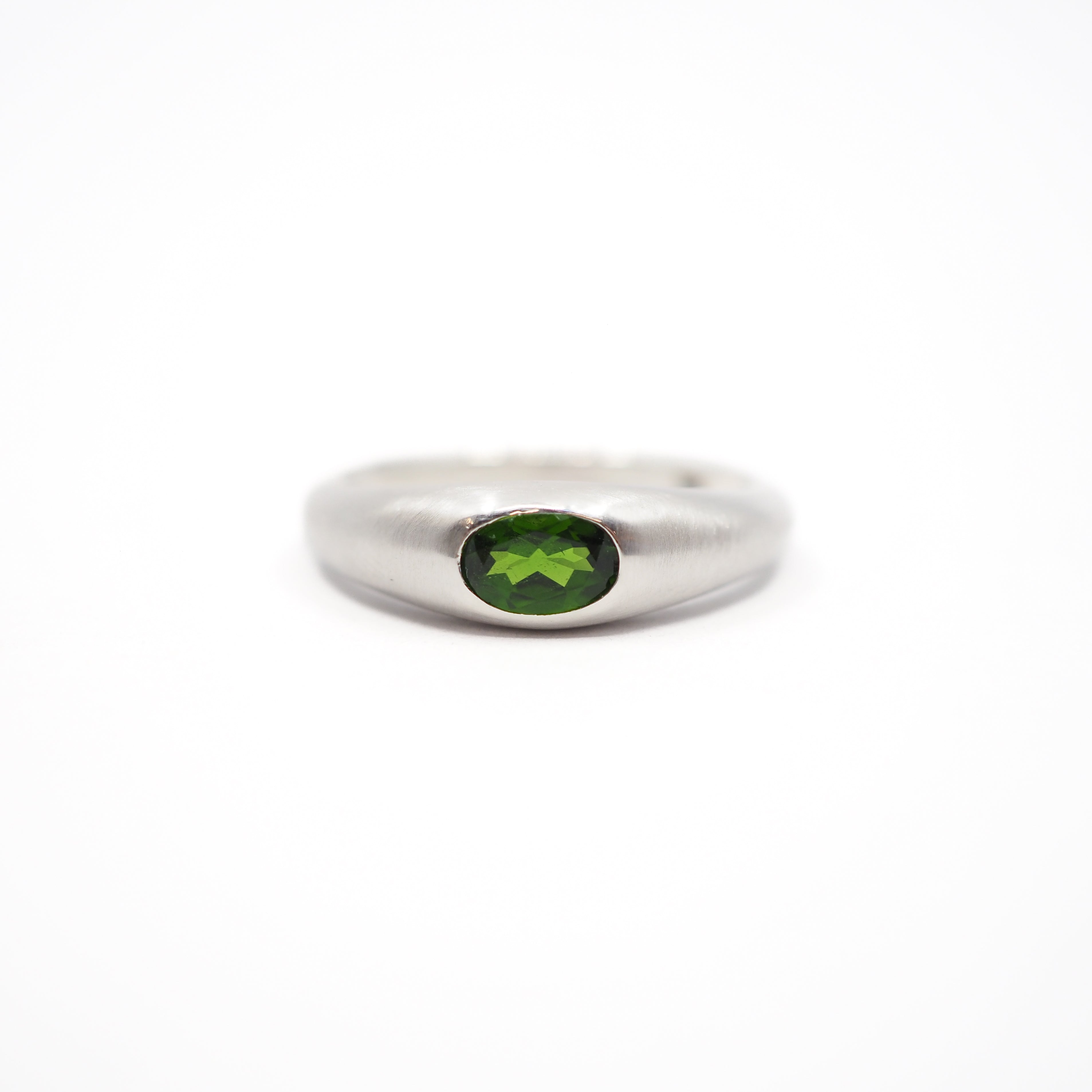 A silver band ring featuring a round green gemstone in a bezel setting, photographed against a seamless white background.