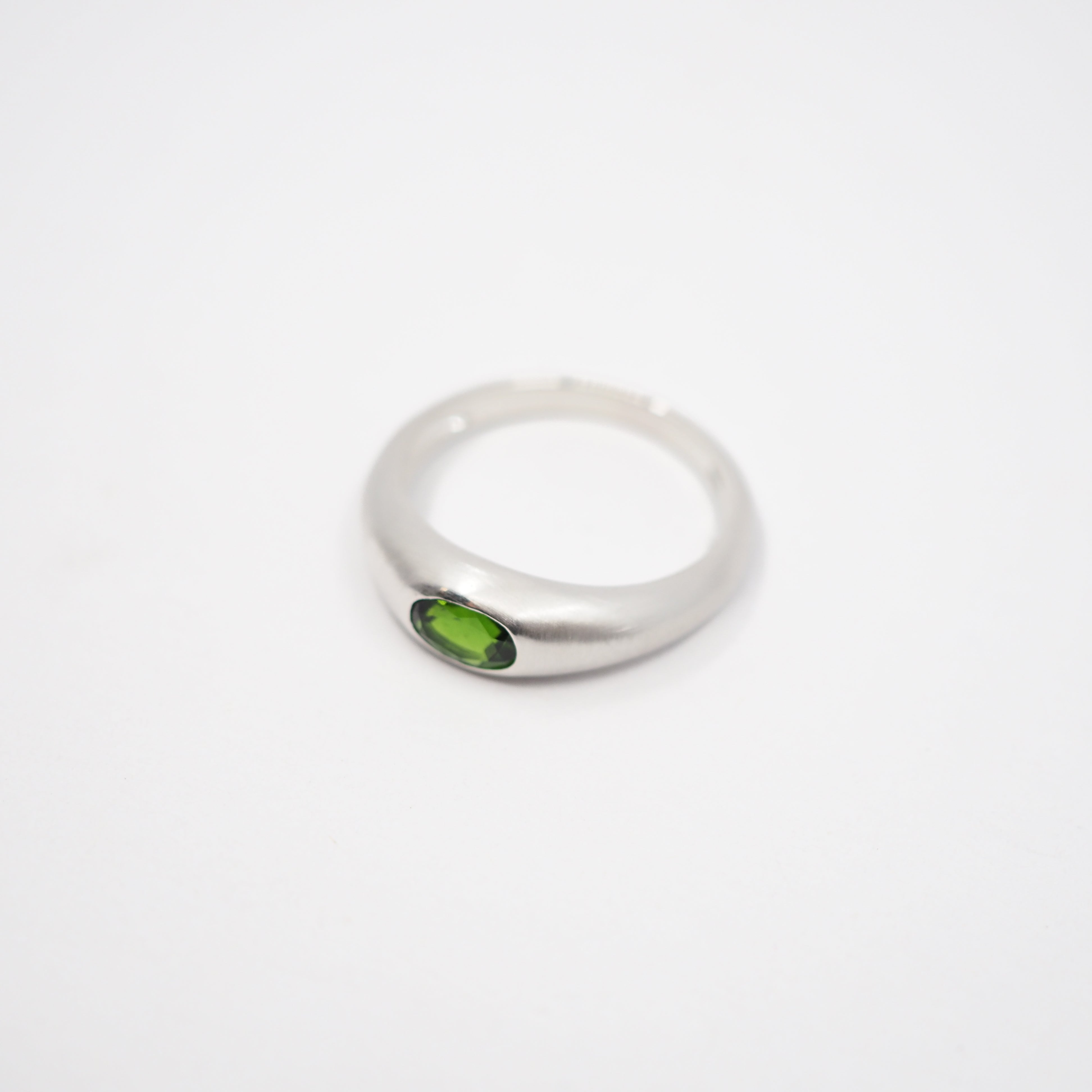 A silver-toned ring with a small oval green gemstone, photographed on a plain white background.