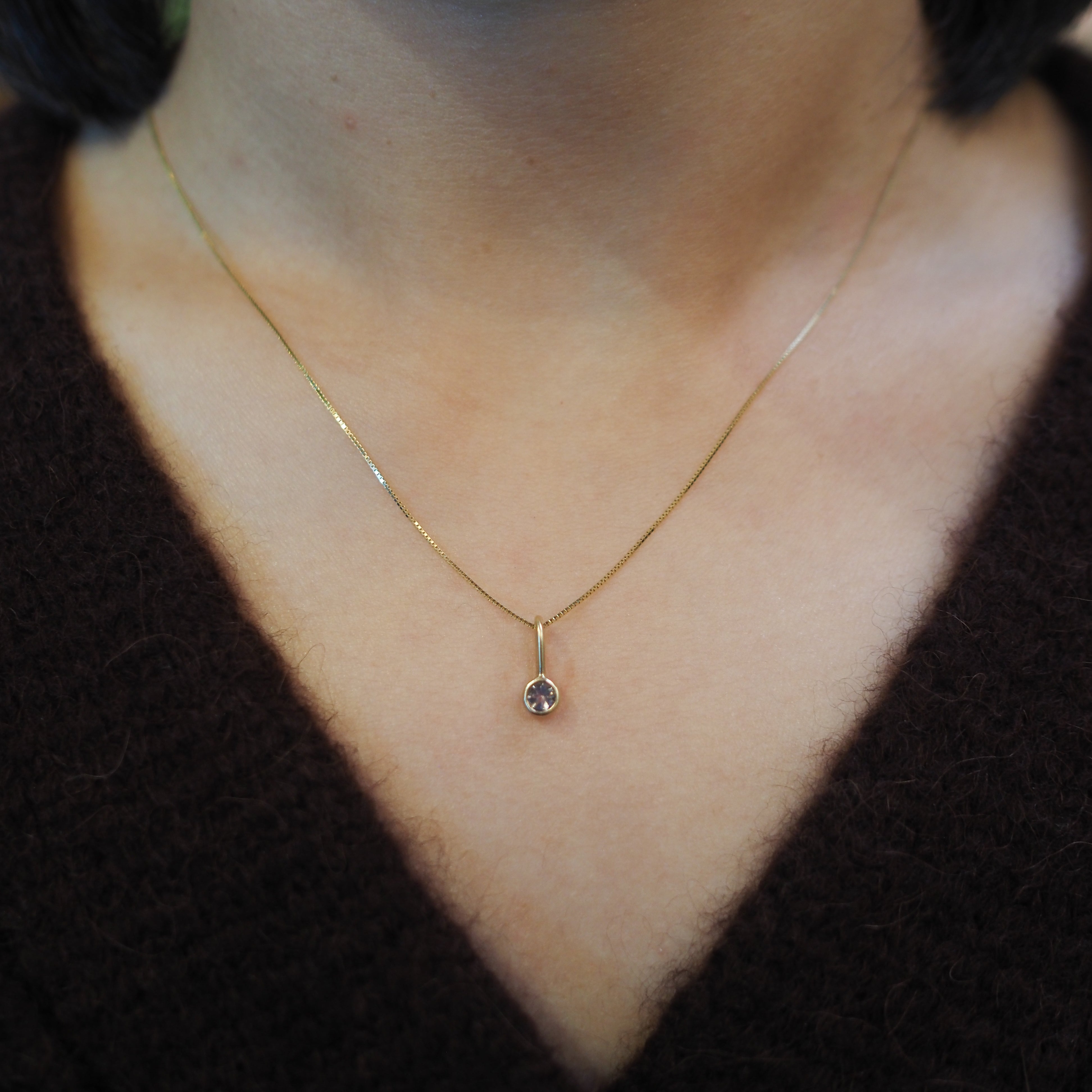 A close-up of a person's neck and chest wearing a delicate gold chain necklace with a small teardrop-shaped clear gemstone pendant.