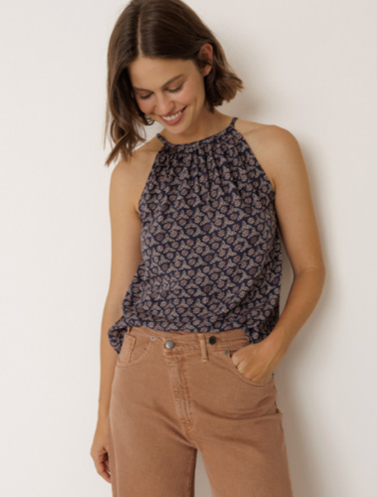 Woman wearing a patterned top and brown pants against a white background