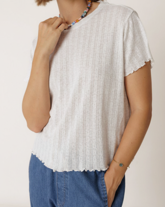 Person wearing a white ribbed t-shirt and blue pants against a plain background