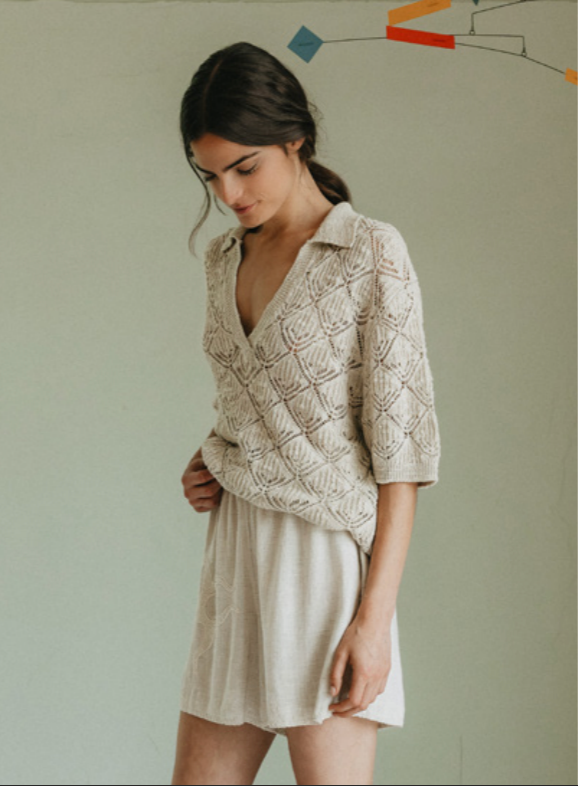 Woman wearing a beige knitted cardigan over a white dress against a plain background