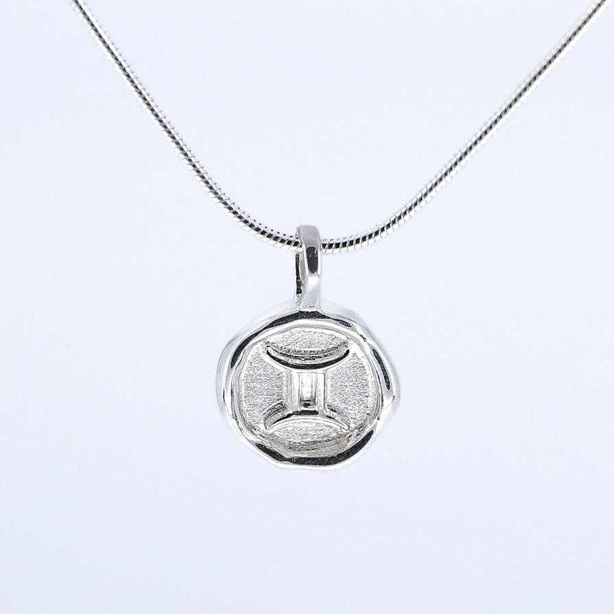 A silver necklace featuring a round pendant with a zodiac sign on it, attached to a delicate chain.